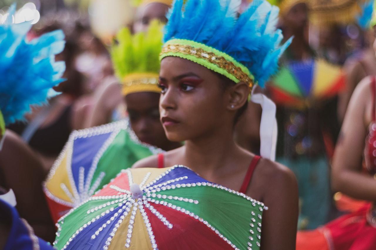 Jovem com cocar de penas azuis e sombrinha de frevo colorida representando a cultura indígena no carnaval